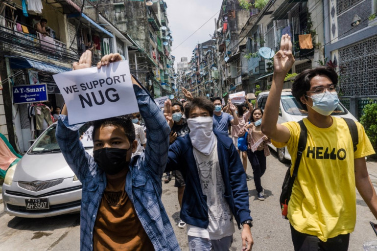 示威者举着支持民族团结政府的标语，抗议者在仰光举行的反军事政变示威游行中做出三指手势（法新社）